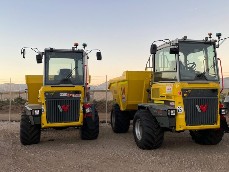 Two Wacker Neuons Dumper Trucks parked on dirt with a sun rise in the background